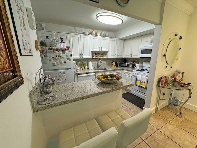 kitchen featuring white appliances, light stone counters, white cabinetry, sink, and kitchen peninsula