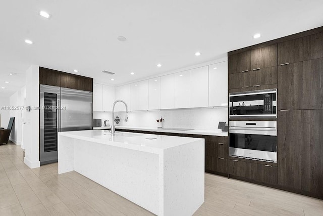 kitchen featuring a center island with sink, built in appliances, sink, and light wood-type flooring