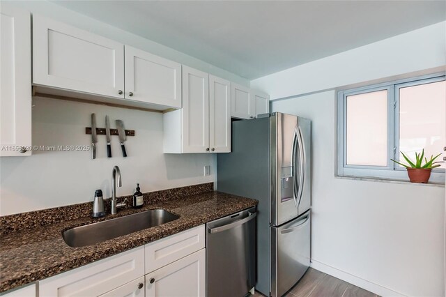 kitchen featuring white cabinets, stainless steel appliances, dark stone counters, and sink