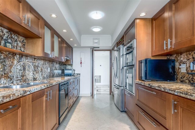 kitchen featuring tasteful backsplash, dishwasher, sink, a raised ceiling, and light stone countertops