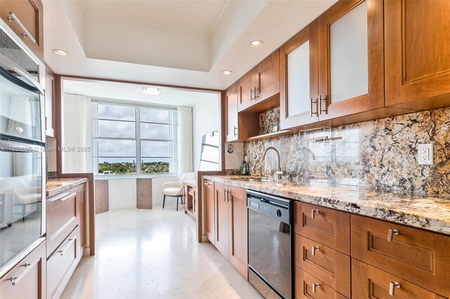 kitchen featuring sink, dishwasher, a tray ceiling, light stone countertops, and decorative backsplash