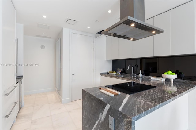 kitchen with black electric cooktop, sink, island exhaust hood, white cabinetry, and dark stone countertops