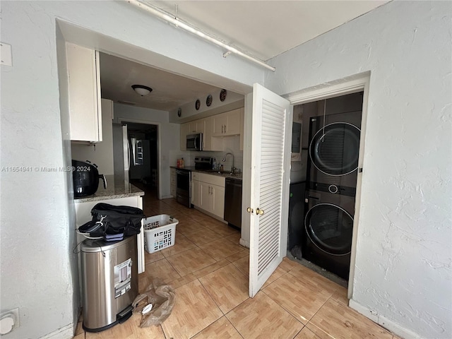 kitchen featuring stainless steel appliances, sink, light tile patterned floors, stacked washer and clothes dryer, and white cabinets