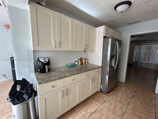 kitchen featuring decorative backsplash, stainless steel refrigerator with ice dispenser, light stone counters, light tile patterned floors, and white cabinetry