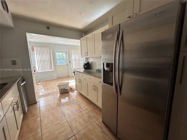 kitchen featuring light tile patterned flooring, backsplash, dark stone counters, white cabinets, and appliances with stainless steel finishes