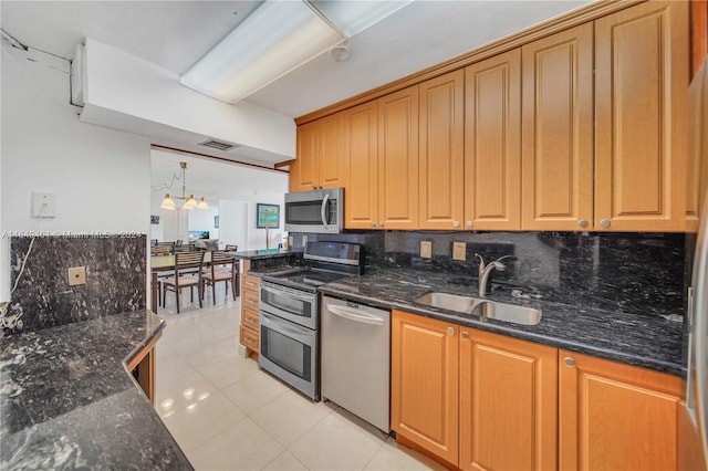 kitchen featuring sink, backsplash, dark stone counters, light tile patterned floors, and appliances with stainless steel finishes