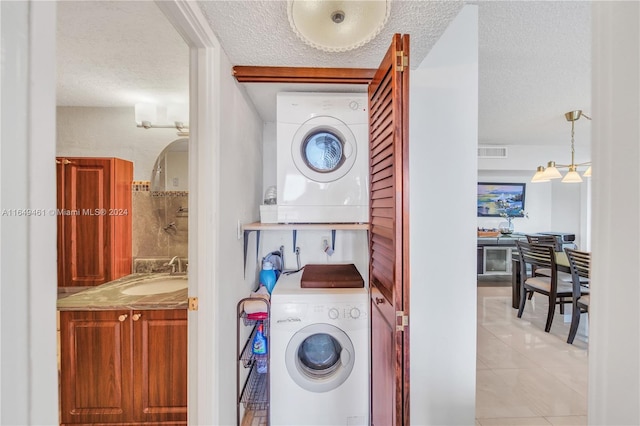 laundry area featuring light tile patterned flooring, a textured ceiling, stacked washing maching and dryer, and sink