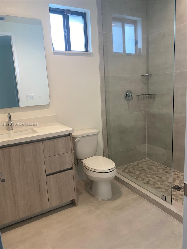 bathroom with tiled shower, vanity, toilet, and tile patterned floors