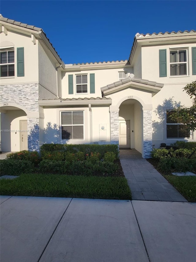 view of front facade featuring a tiled roof, stone siding, and stucco siding