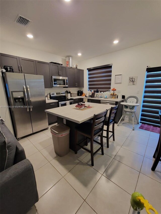 kitchen featuring a kitchen island, stainless steel appliances, a breakfast bar, and light tile patterned floors