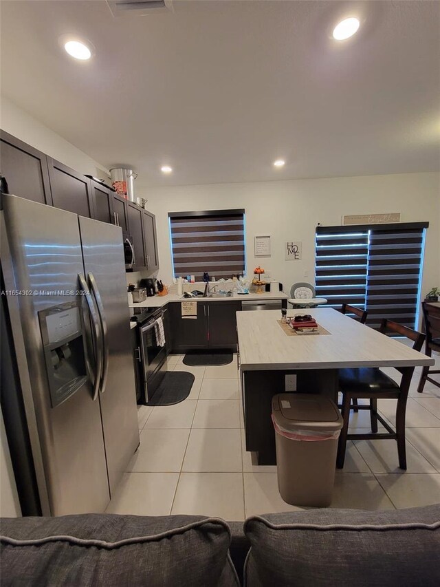 kitchen featuring a kitchen island, light tile patterned floors, appliances with stainless steel finishes, a breakfast bar, and sink