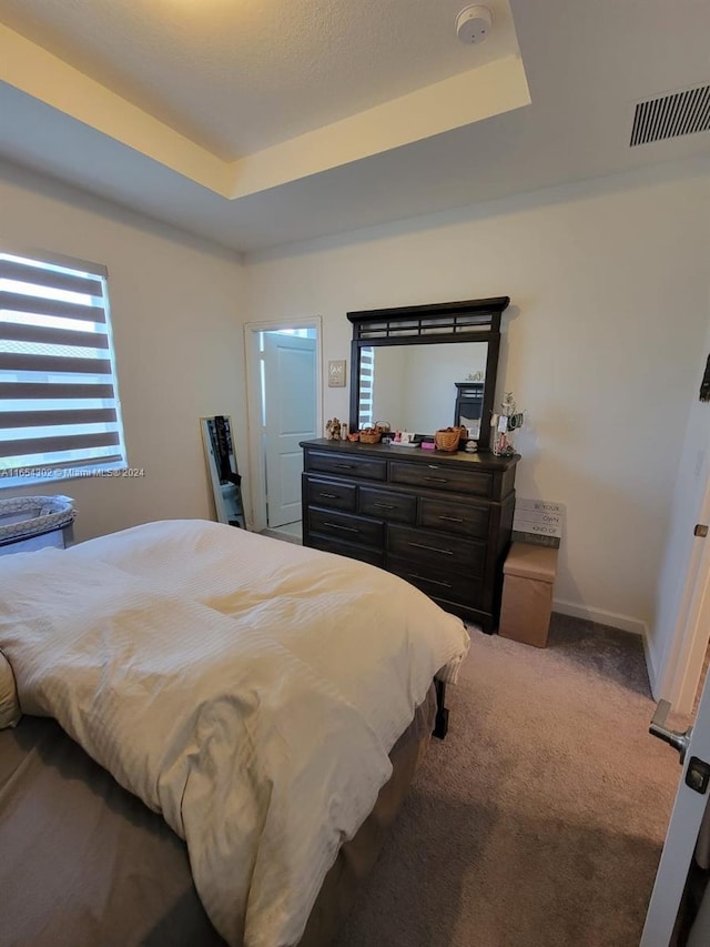 bedroom with a tray ceiling, baseboards, visible vents, and carpet flooring