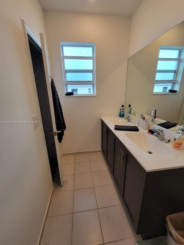 full bath featuring tile patterned flooring, double vanity, baseboards, and a sink