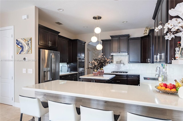 kitchen featuring stainless steel appliances, sink, dark brown cabinets, kitchen peninsula, and a breakfast bar