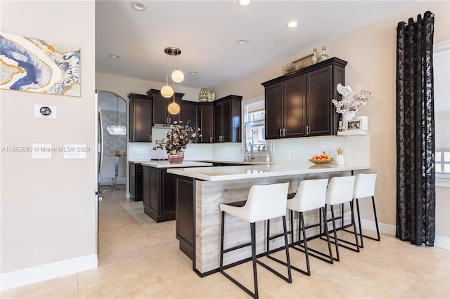 kitchen featuring dark brown cabinets, kitchen peninsula, decorative backsplash, hanging light fixtures, and a breakfast bar