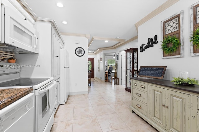 kitchen with crown molding, white appliances, light tile patterned floors, and cream cabinetry