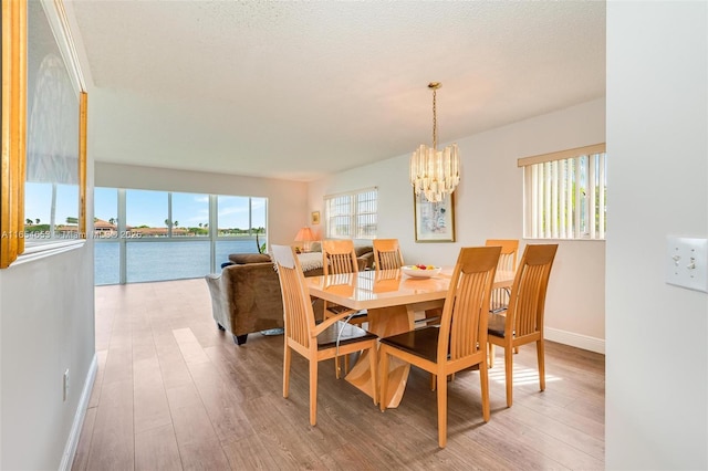 dining space with baseboards, wood finished floors, a water view, an inviting chandelier, and a textured ceiling