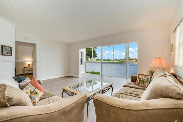 living room with a textured ceiling, a water view, wood finished floors, and baseboards