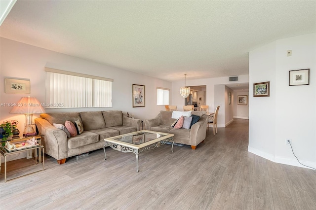 living area with a chandelier, visible vents, light wood-style flooring, and a textured ceiling