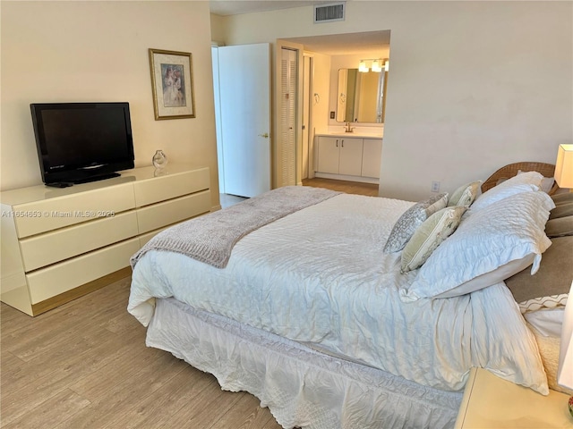 bedroom featuring ensuite bathroom, light wood-style flooring, visible vents, and an inviting chandelier