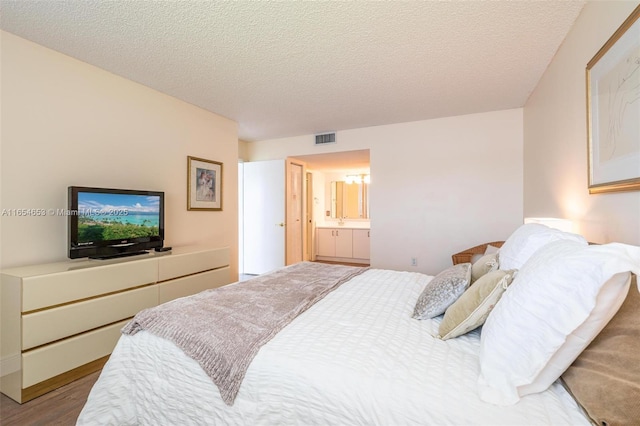 bedroom featuring ensuite bath, a textured ceiling, and light hardwood / wood-style floors