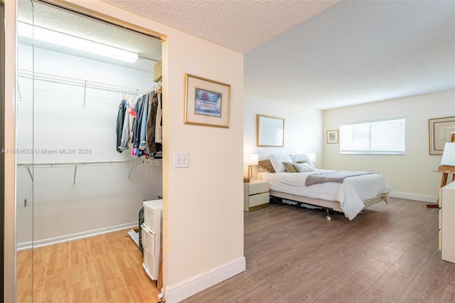 bedroom with a textured ceiling, a closet, light wood-type flooring, and baseboards