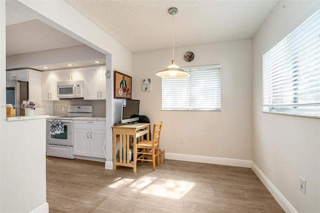 kitchen with light wood-type flooring, white cabinetry, hanging light fixtures, and white appliances