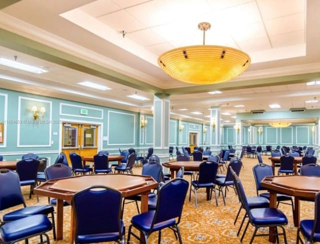 dining area with ornate columns, a raised ceiling, crown molding, and a decorative wall