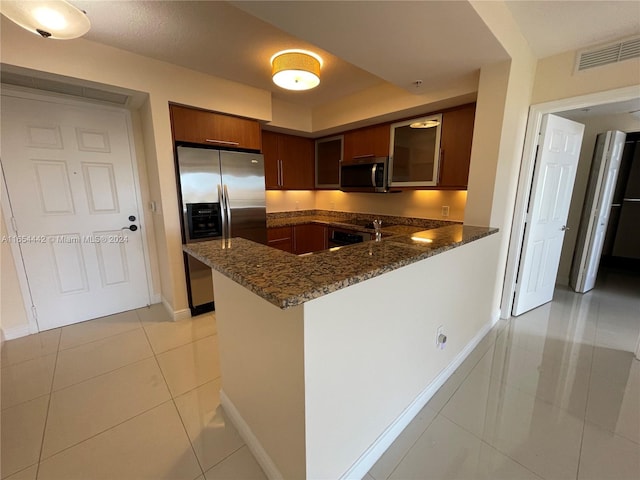 kitchen with light tile patterned flooring, stainless steel appliances, kitchen peninsula, and dark stone counters