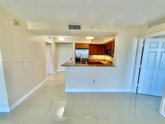 kitchen with dark stone countertops, light tile patterned floors, appliances with stainless steel finishes, and kitchen peninsula