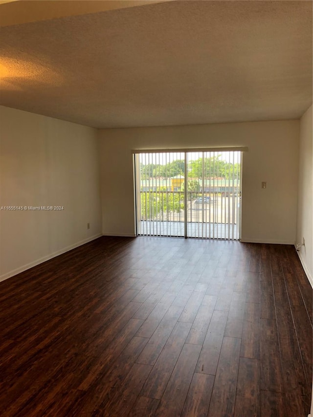 empty room with a textured ceiling, a healthy amount of sunlight, and dark hardwood / wood-style floors