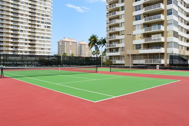 view of tennis court featuring community basketball court, fence, and a city view