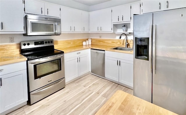 kitchen with appliances with stainless steel finishes, light wood-type flooring, sink, and white cabinetry