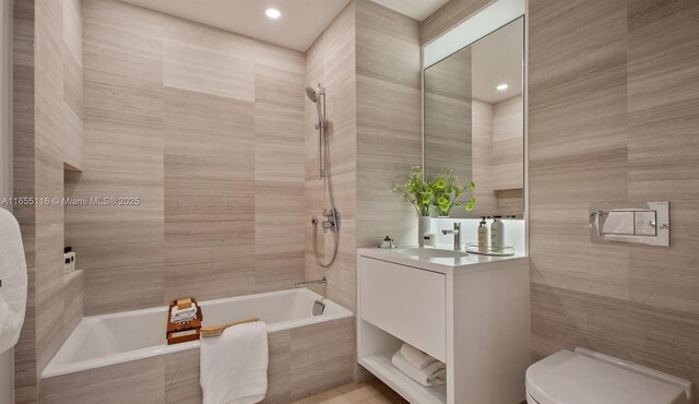 full bathroom with toilet, tiled shower / bath, vanity, and tile walls