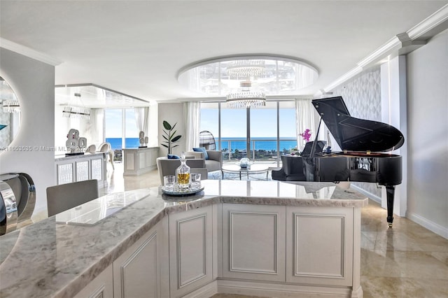 kitchen featuring light stone counters, a notable chandelier, white cabinetry, a water view, and ornamental molding