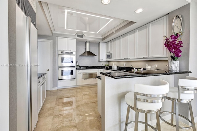 kitchen with visible vents, built in appliances, a peninsula, a warming drawer, and wall chimney exhaust hood
