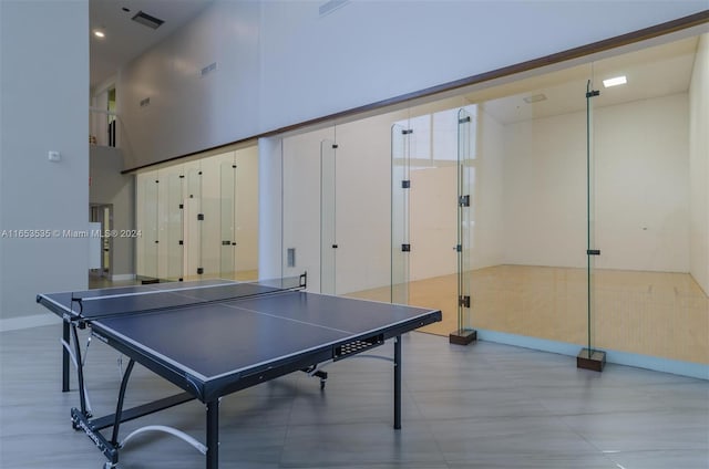 recreation room with baseboards, a high ceiling, and visible vents