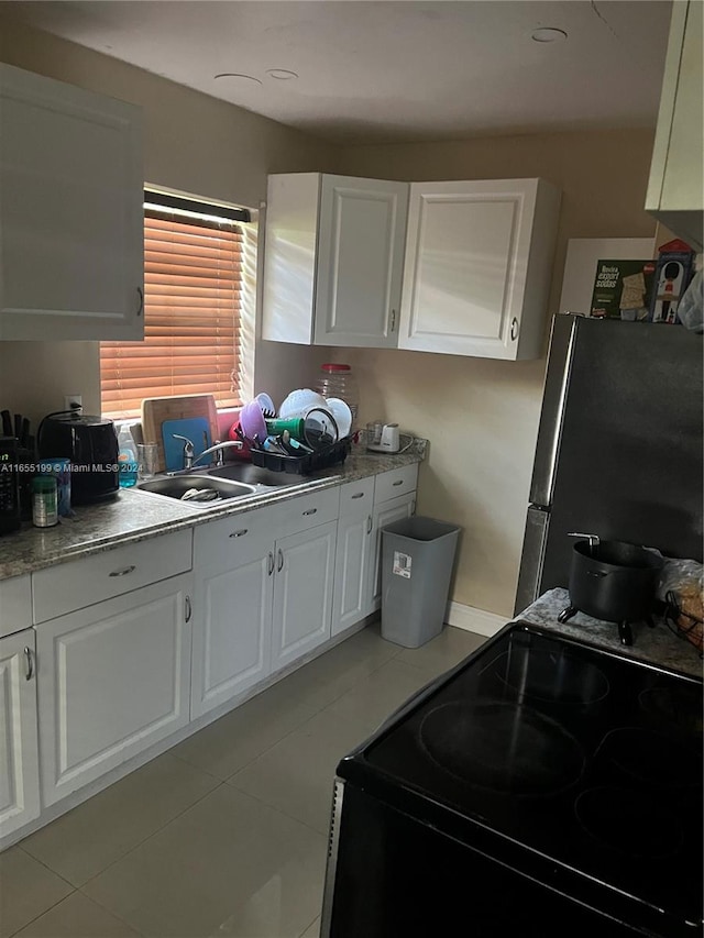 kitchen with stainless steel refrigerator, sink, white cabinetry, black range with electric cooktop, and light tile patterned flooring