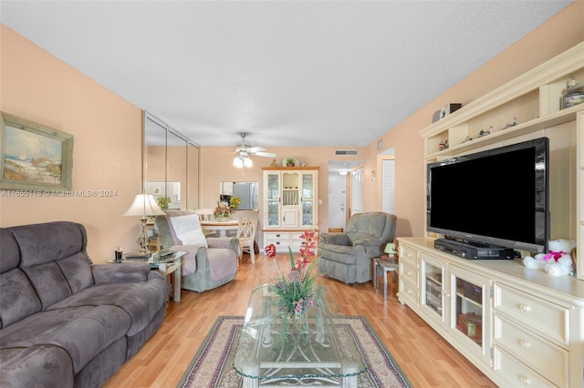 living room featuring light wood-type flooring, a textured ceiling, and ceiling fan