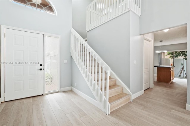 entryway with a textured ceiling, light hardwood / wood-style floors, and a high ceiling