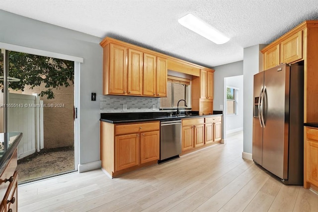 kitchen featuring decorative backsplash, light wood-type flooring, a textured ceiling, stainless steel appliances, and sink