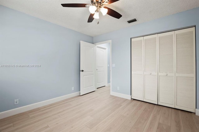 unfurnished bedroom featuring a textured ceiling, a closet, light hardwood / wood-style flooring, and ceiling fan