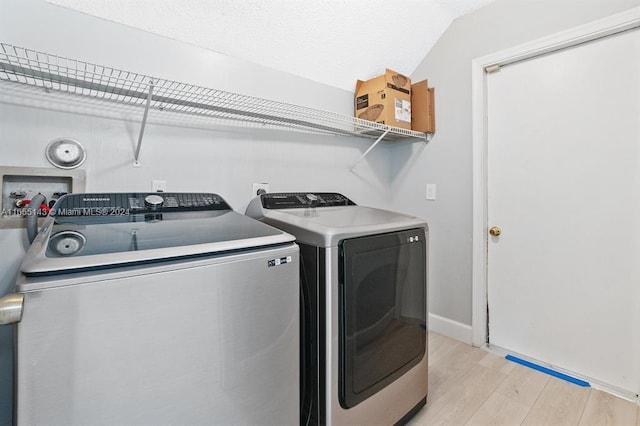 clothes washing area with washing machine and clothes dryer and light hardwood / wood-style flooring