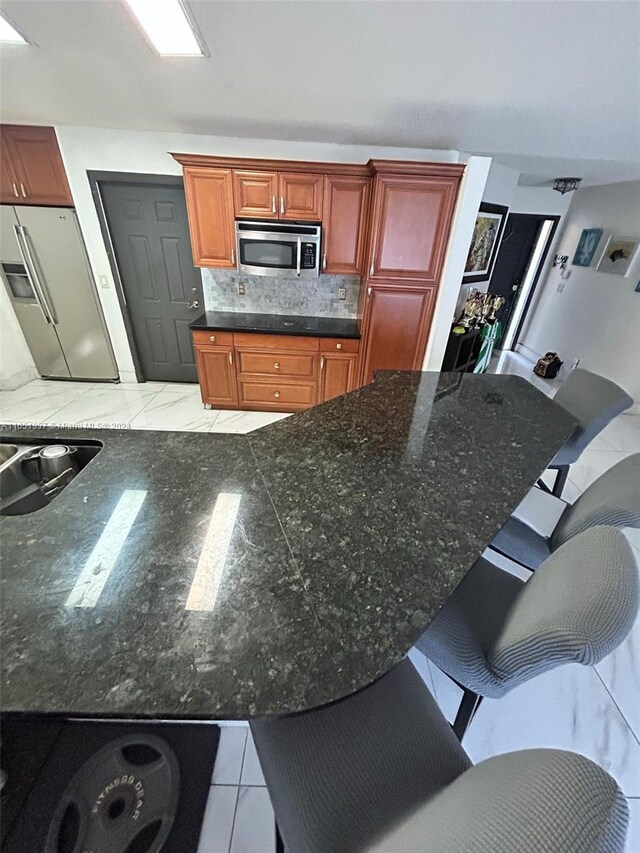 kitchen with kitchen peninsula, appliances with stainless steel finishes, a kitchen bar, and decorative backsplash