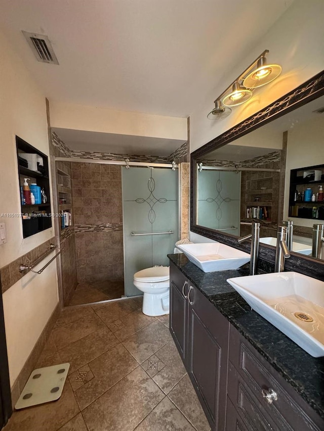 bathroom featuring toilet, vanity, a tile shower, and tile patterned flooring