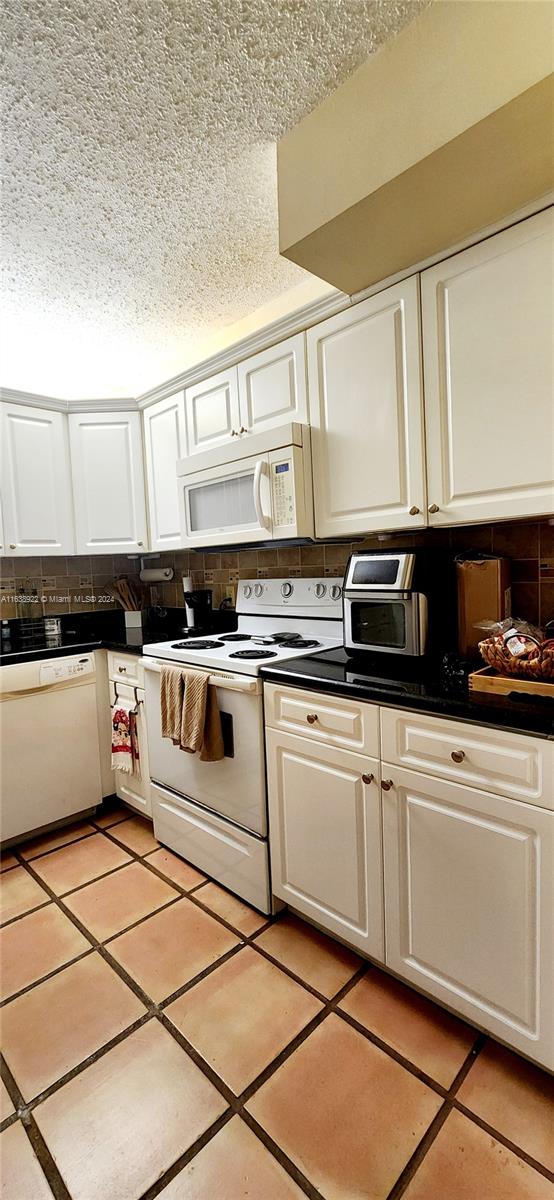 kitchen featuring a textured ceiling, light tile patterned floors, white appliances, and white cabinets