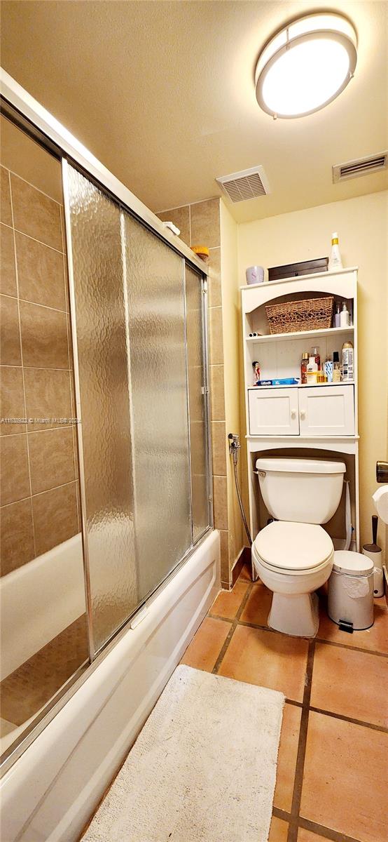 bathroom featuring tile patterned flooring, toilet, and combined bath / shower with glass door