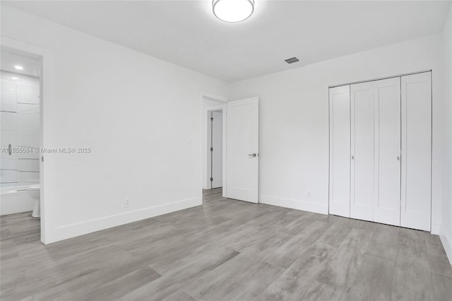 unfurnished bedroom with ensuite bath, a closet, and light hardwood / wood-style flooring