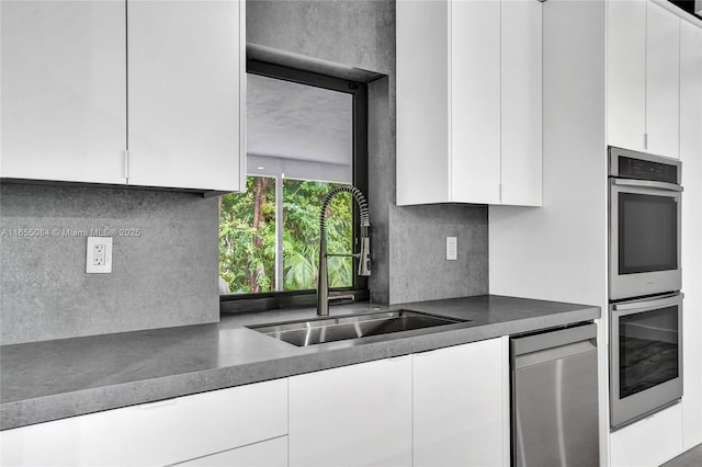 kitchen with tasteful backsplash, white cabinets, appliances with stainless steel finishes, and sink