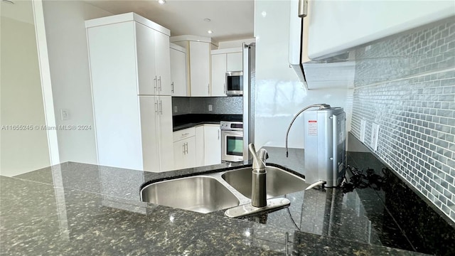 kitchen with white cabinets, appliances with stainless steel finishes, tasteful backsplash, and dark stone counters